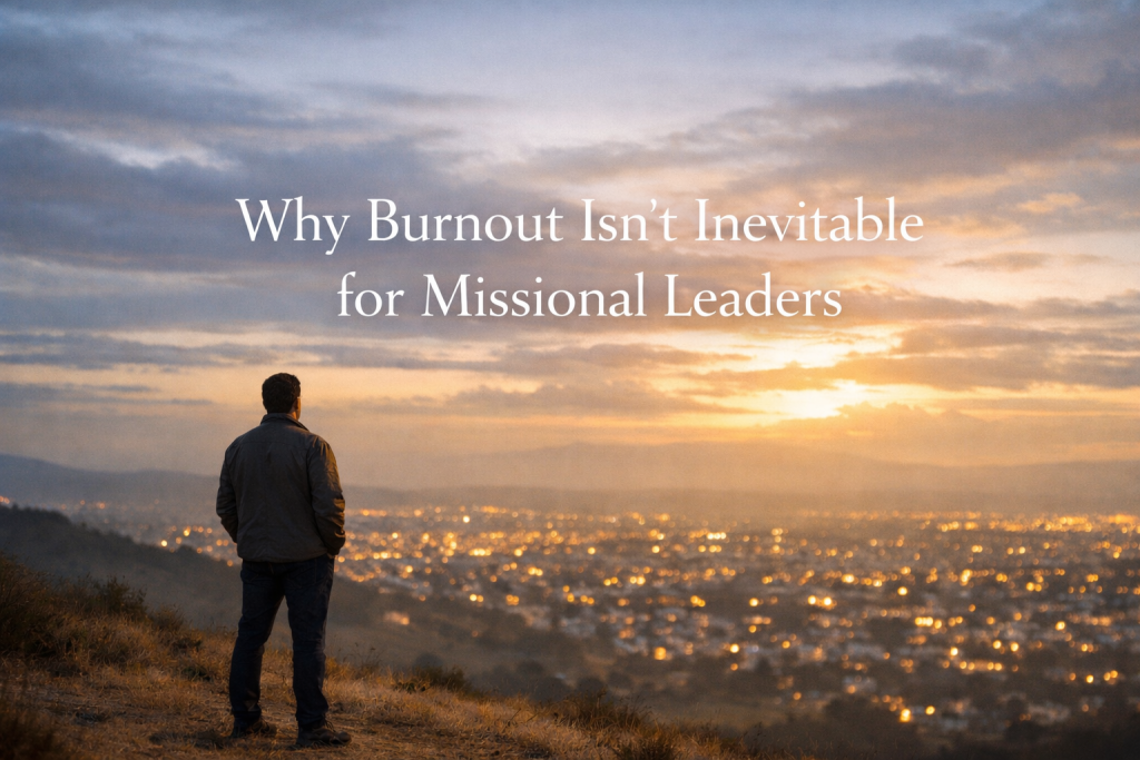 A solitary leader stands on a hillside overlooking a softly glowing city at dawn or dusk, under a wide sky with warm light breaking through clouds. The scene feels calm and contemplative, with large centered text reading, “Why Burnout Isn’t Inevitable for Missional Leaders.”